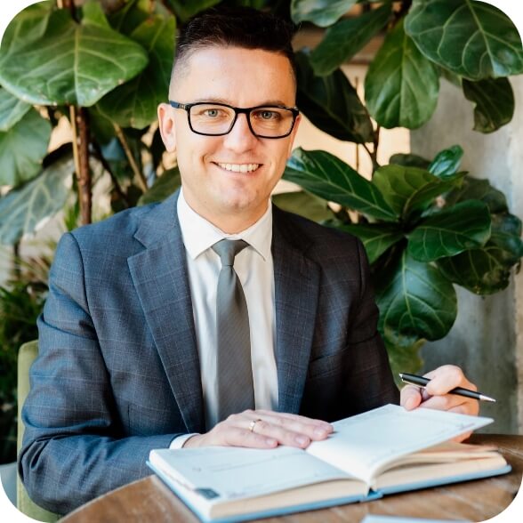 Piotr Grudniewski siedzi przy stole. Na stole leży kalendarz