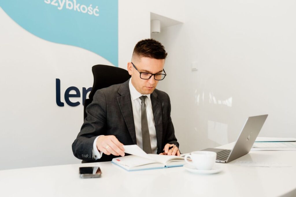 Piotr Grudniewski siedzi przy biurku przy otwartym laptopie i umawia spotkanie z klientem