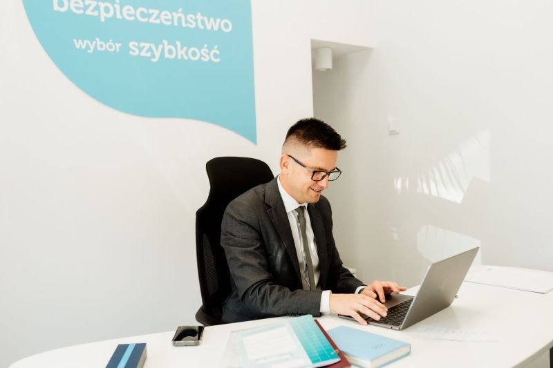 Piotr Grudniewski siedzi przy biurku przy otwartym laptopie